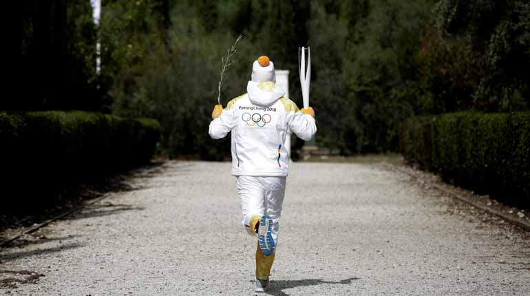 Man iklädd vinterkläder med texten PyeongChang 2018 springer iväg bort från kameran med en brinnande fackla.