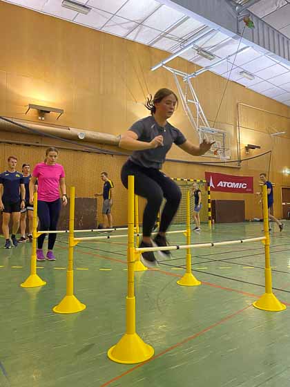 Flicka som hoppar över uppställda häckar i en gymnastikhall.