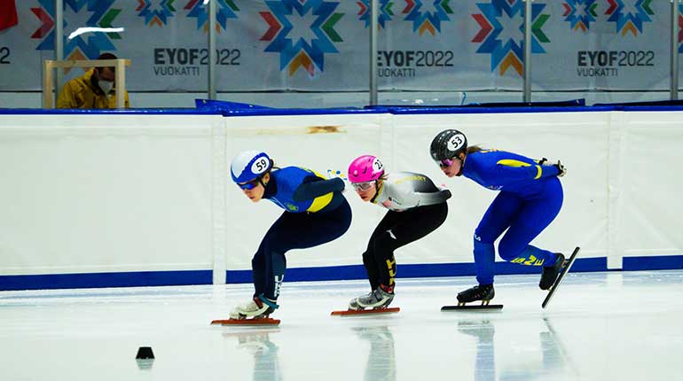 Tre short track åkare i en kurva efter varandra.