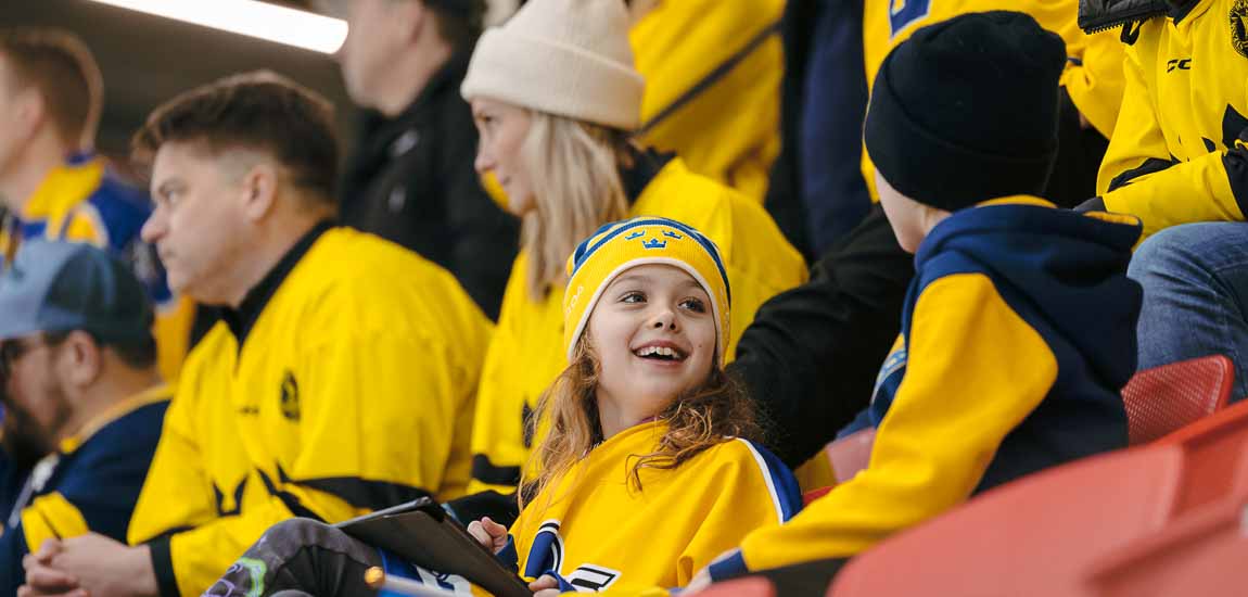 En flicka ler i publik med svenska hockeytröjor.