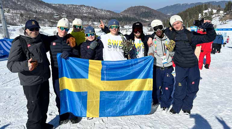 Ett gäng glada ungdomar bakom en svensk flagga i skidbacken.