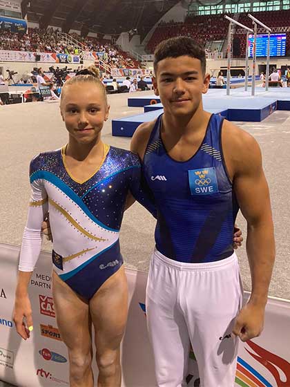 Två gymnaster i svenska tävlingsdräkter framför podiet.