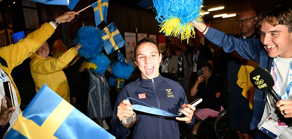 Svenska flaggor och jublande människor hyllar Tara Babulfath som strålar med en bronsmedalj i handen. 
