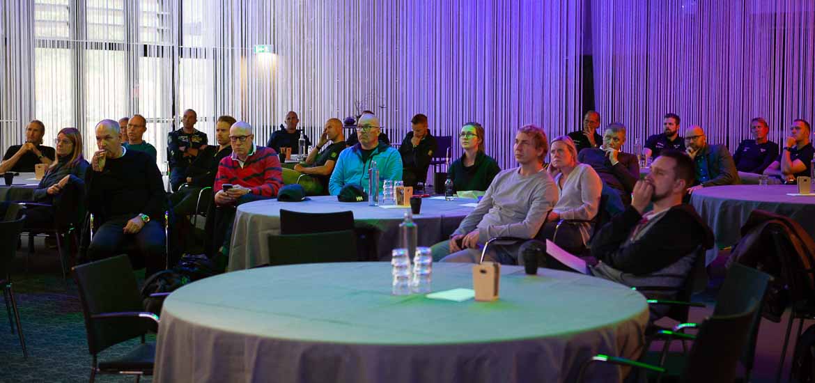 En samling människor som sitter utspridda kring runda bord.